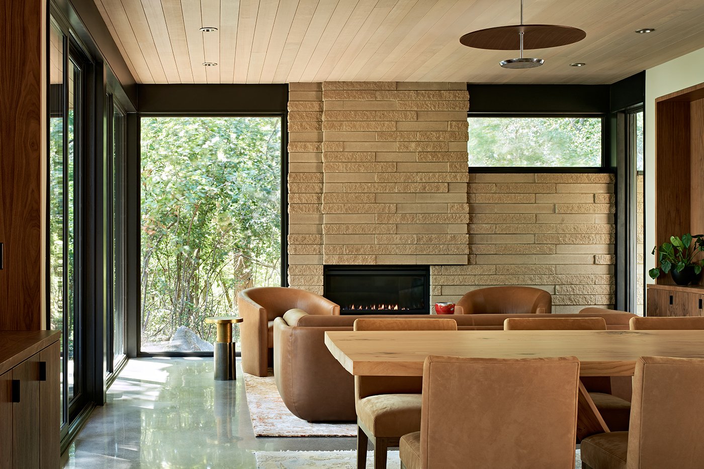 A living room with corner windows that stretch floor to ceiling and a stonework fireplace.