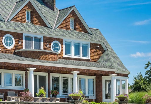 A two-story home with brown shingles, a porch with white columns, and white windows. 