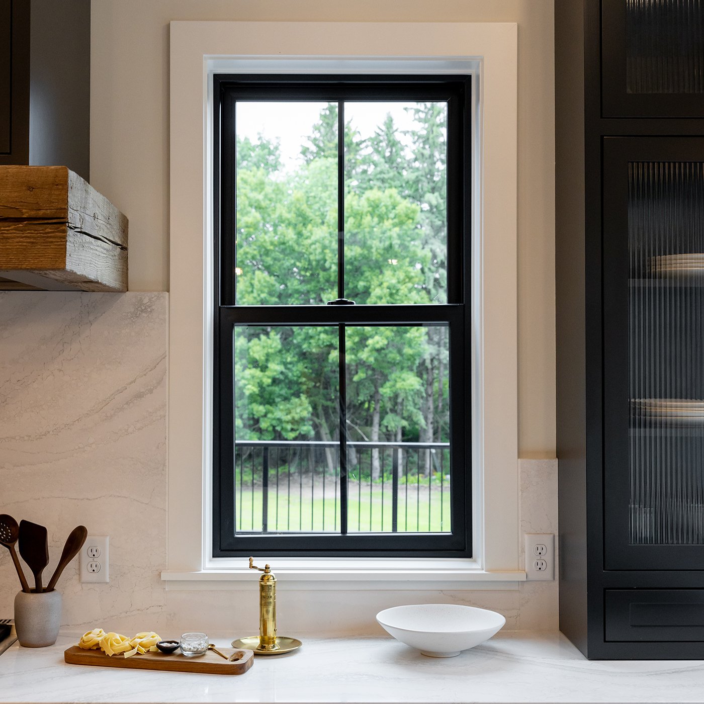 A kitchen with black cabinetry, quartz countertops and backsplash, and a black-framed Andersen® 100 Series Single-Hung Window.