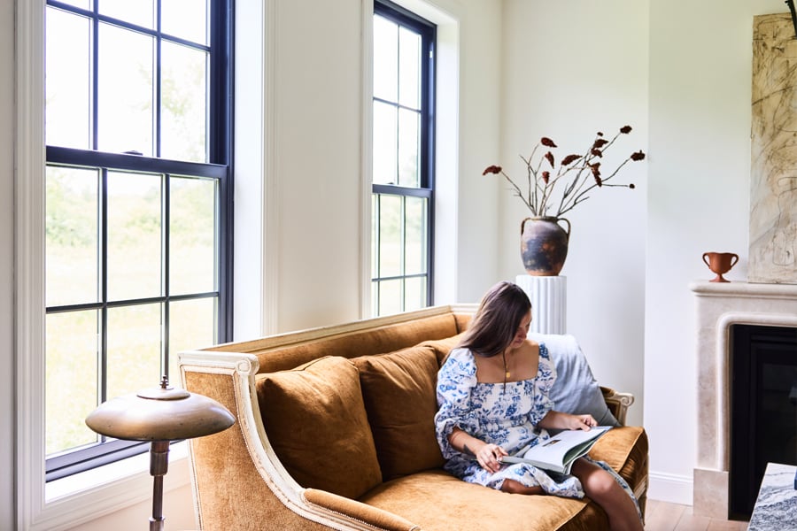 A living room awash in light coming through two tall Andersen® 100 Series Single-Hung Windows.