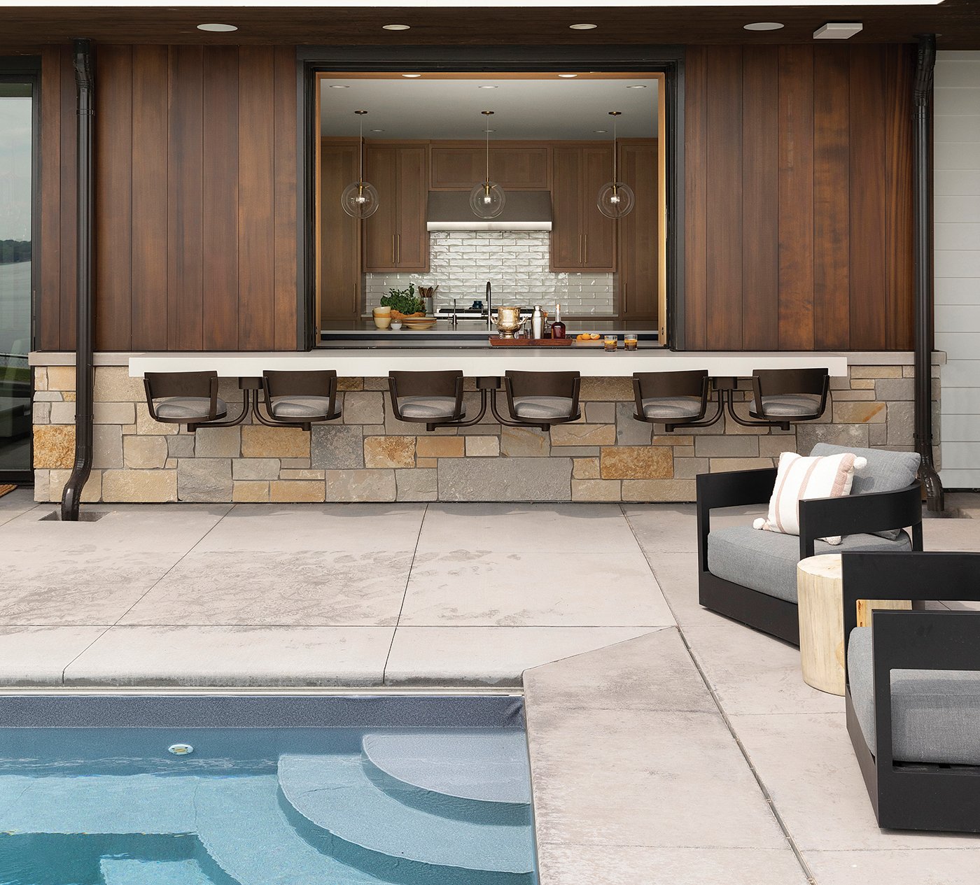 An open pass-through window connects a kitchen with a concrete patio and outdoor pool.