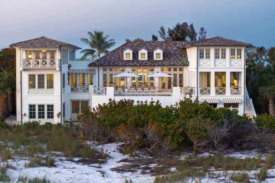 An outside shot taken from the beach of a two-story transitional home with white walls and balconies wrapping around the entire second floor. 