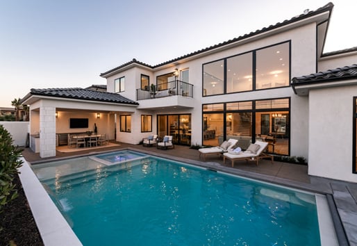 An outdoor dining area next to an underground pool with large, black windows and doors allowing deck access