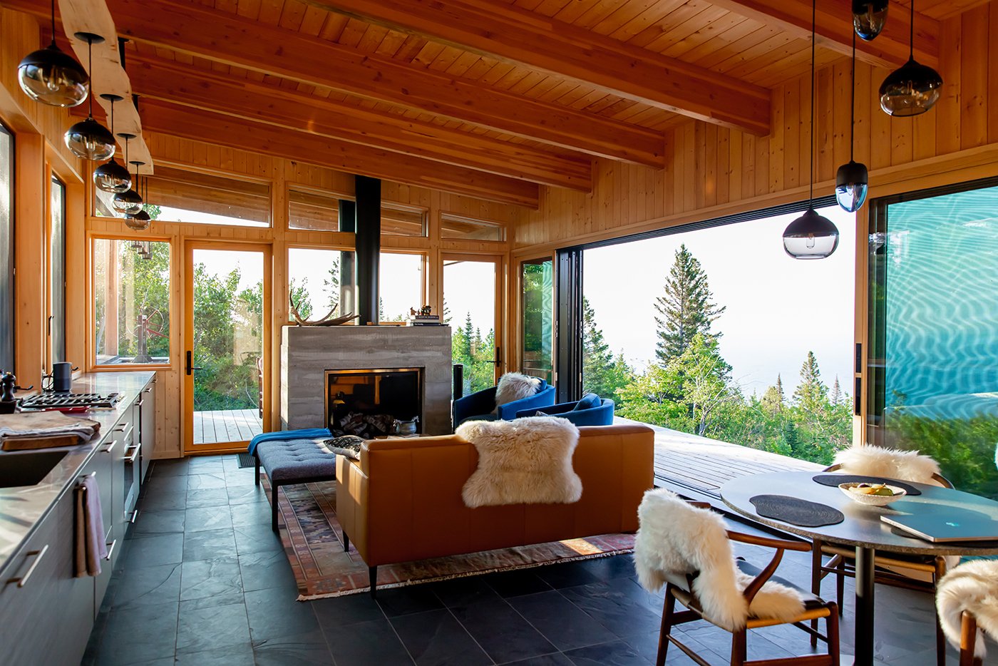 Interior view of a modern cabin with large, glass Andersen windows nestled in the north woods and an Andersen MultiGlide Door opening an entire wall to the landscape and Lake Superior views beyond. 