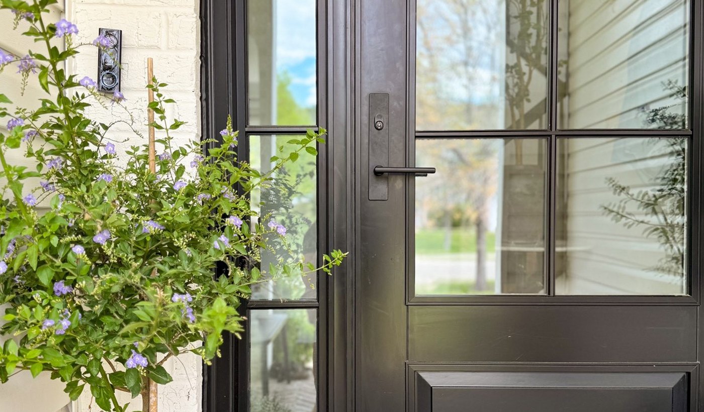 A modern front door with a light-colored wood exterior and horizontal glass panels popping against the white brick walls of a Mid-Century Modern home.